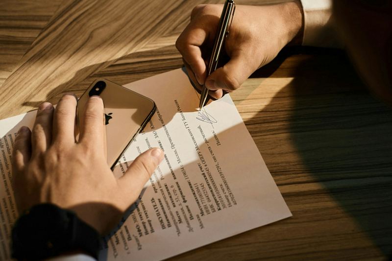 Mão assinando um documento sobre uma mesa de madeira
